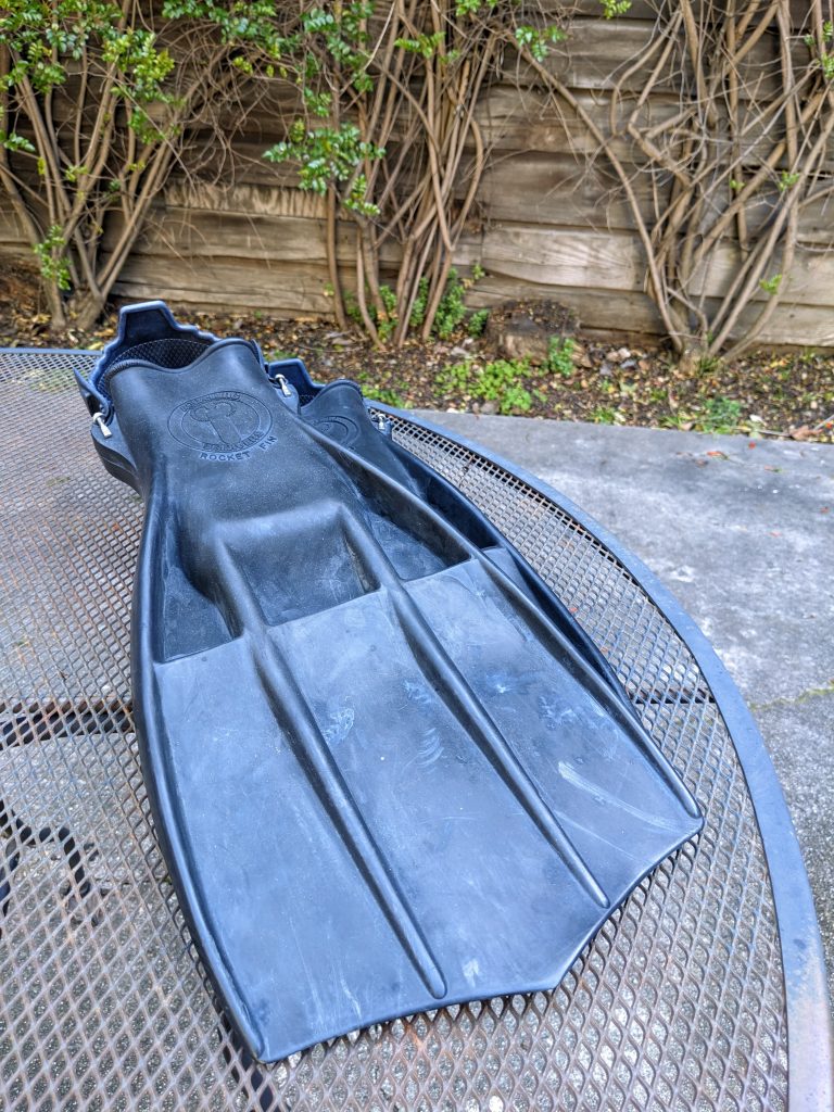 A pair of black diving fins, open heel design, on a table top.