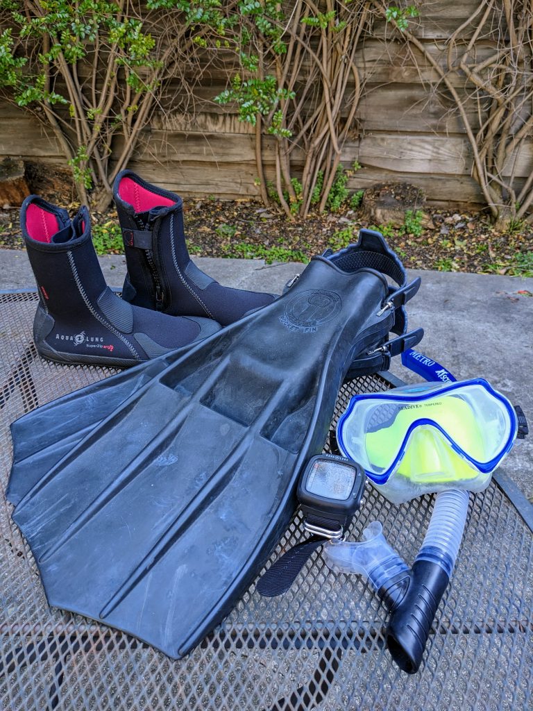 Scuba boots, fins, mask, snorkel, dive computer laid out on a table