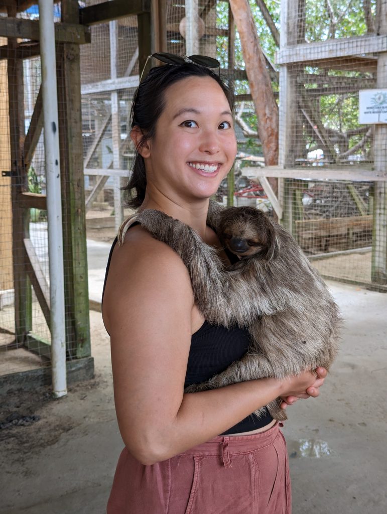 An asian woman is holding a sloth with both hands. 
